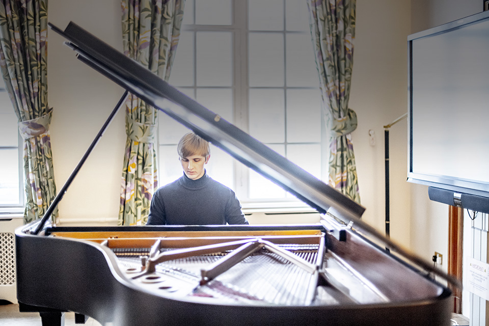 A male pianist, playing the piano in a well-lit room.
